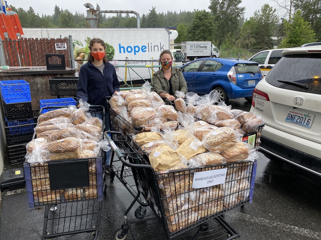 Two people stand behind two shopping carts filled with loaves of bread in a food bank parking lot